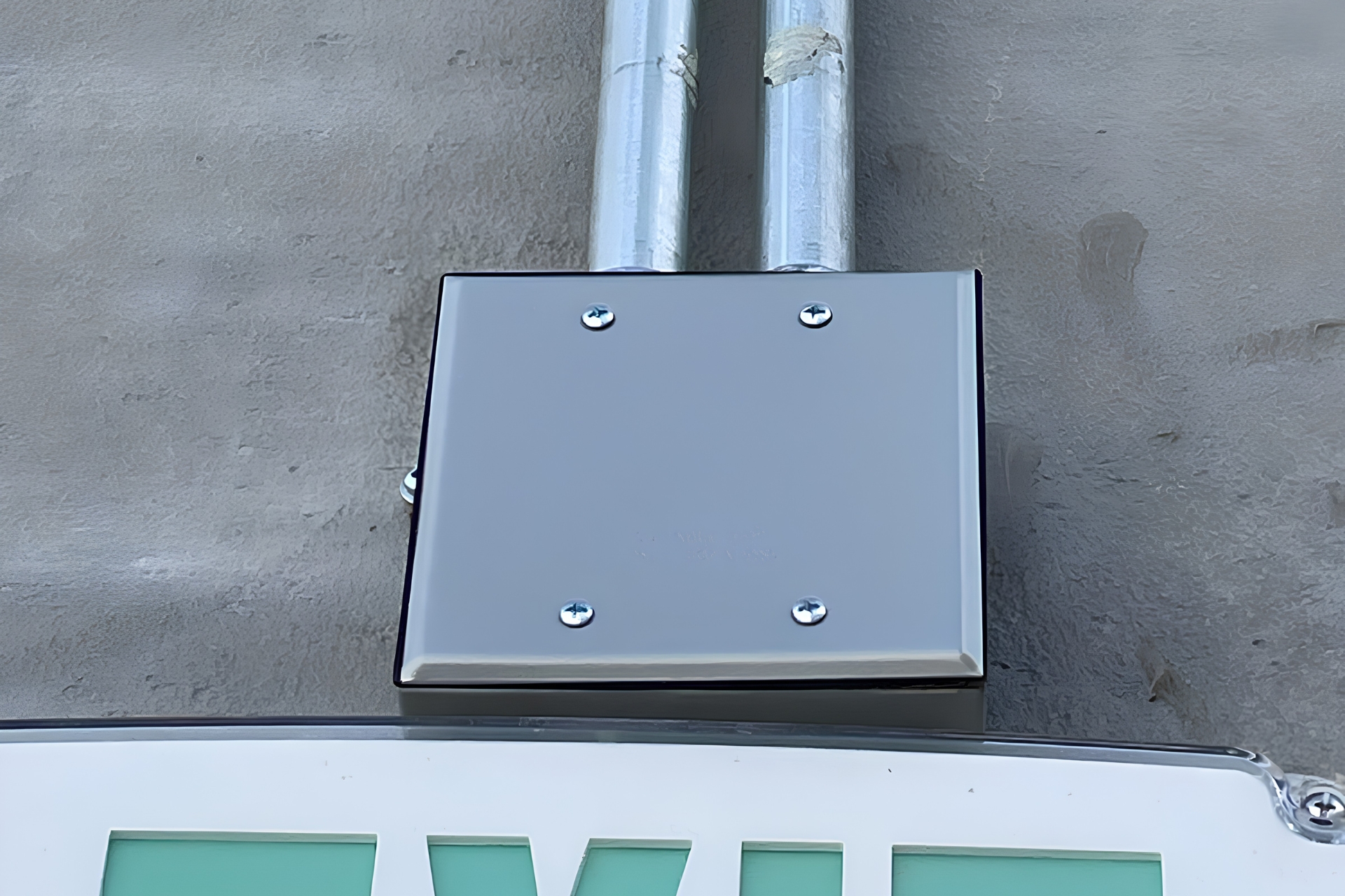 Metal junction box with two vertical conduit pipes mounted on a textured gray wall.