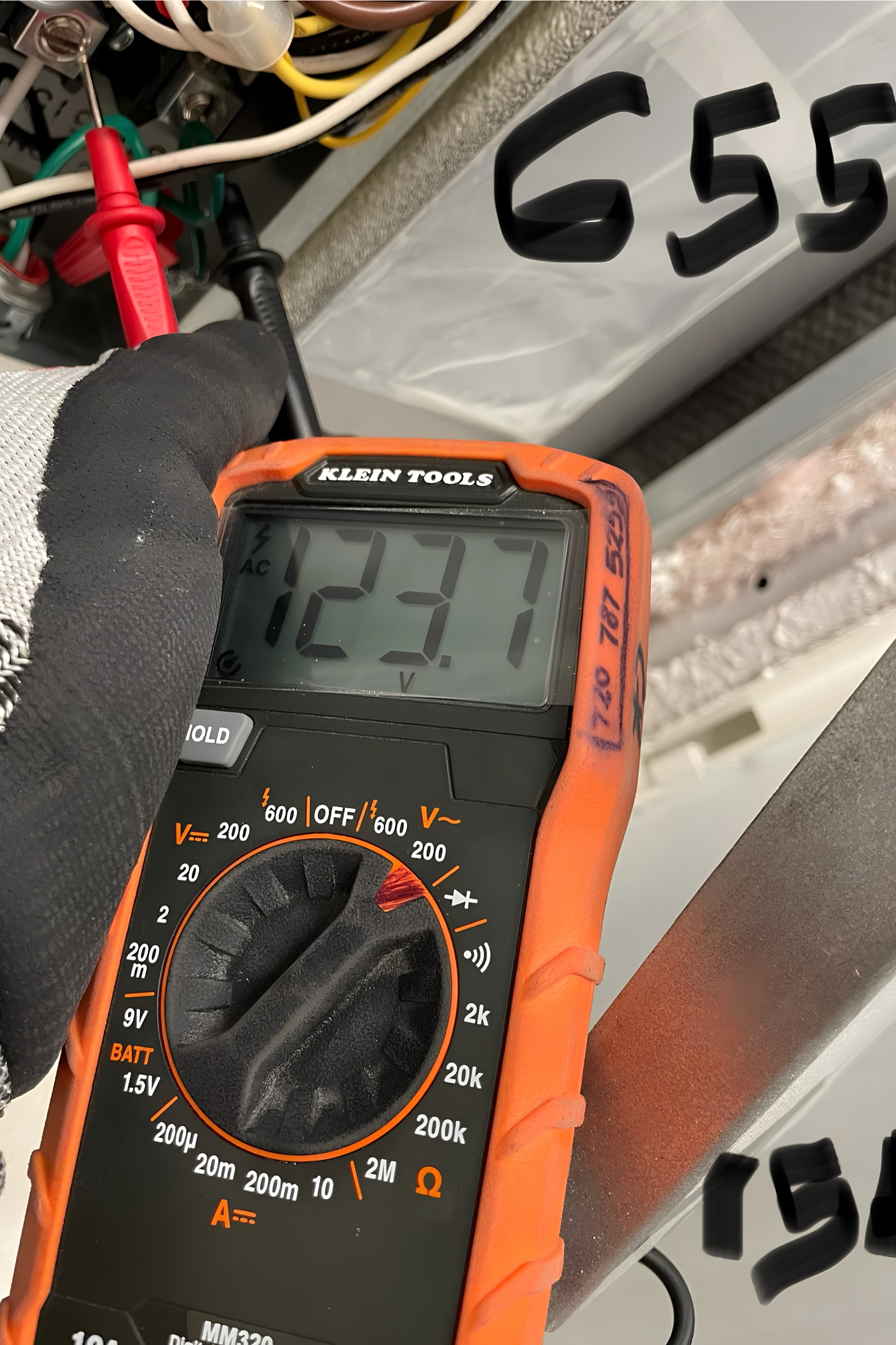 Gloved hand using a digital multimeter to test wiring inside an electrical panel.