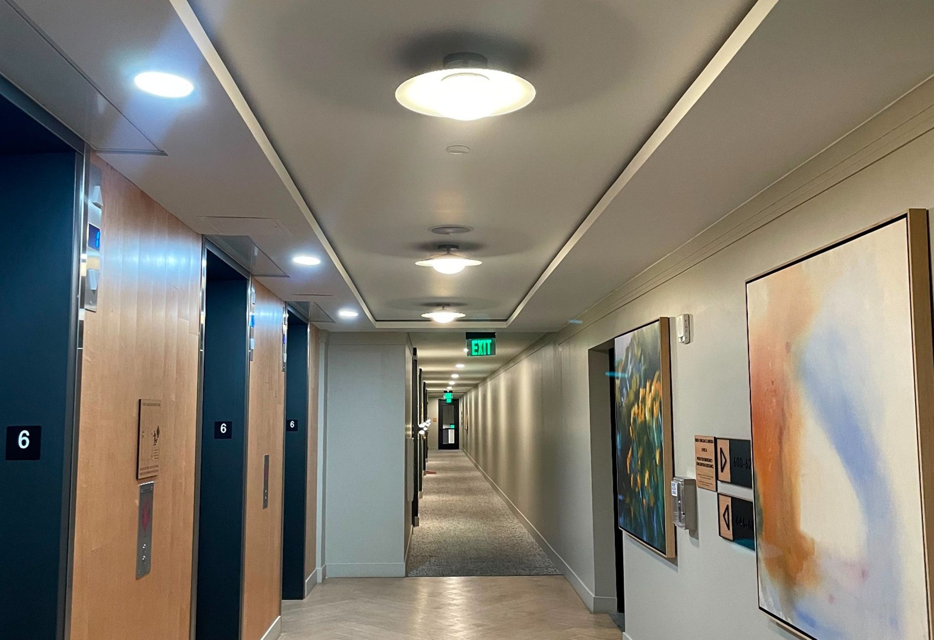 Interior corridor with ceiling lighting and an illuminated exit sign.